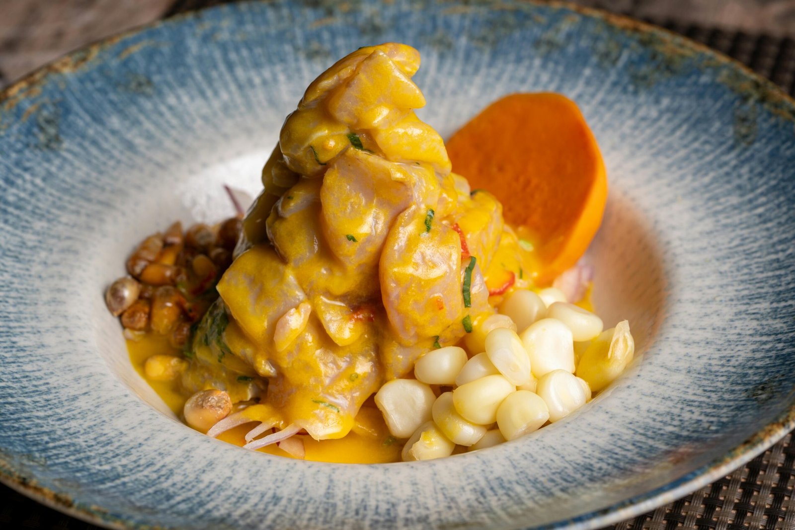 A vibrant dish of Peruvian ceviche featuring corn and sweet potato on a decorative blue plate.